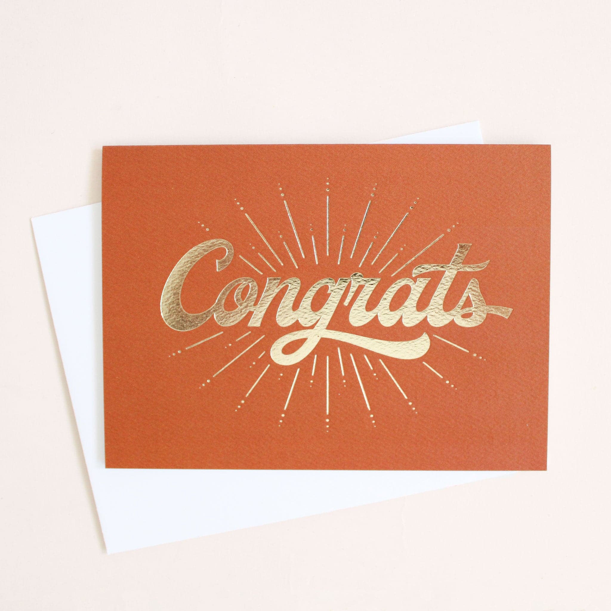 deep orange colored greeting card with a gold foil starburst design surrounding the word congrats.