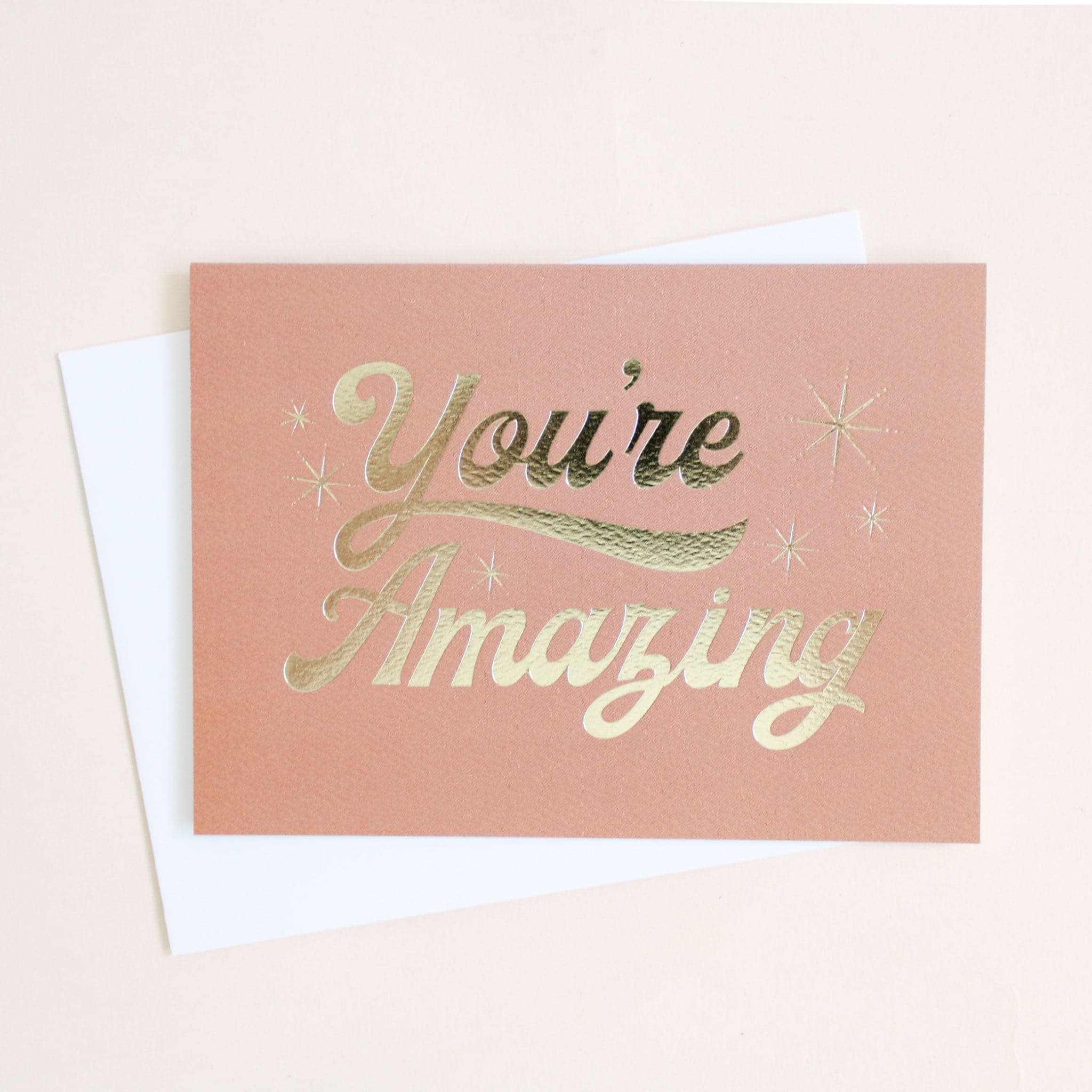 This soft pink card reads in &#39;You&#39;re Amazing&#39; in shimmering, gold foil surrounded by six twinkling stars. This card is accompanied by a white envelope. 