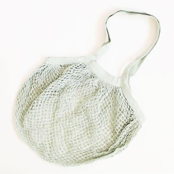 On a cream background is a mint green woven mesh shopping bag with a diamond pattern and two over the shoulder handle straps. 