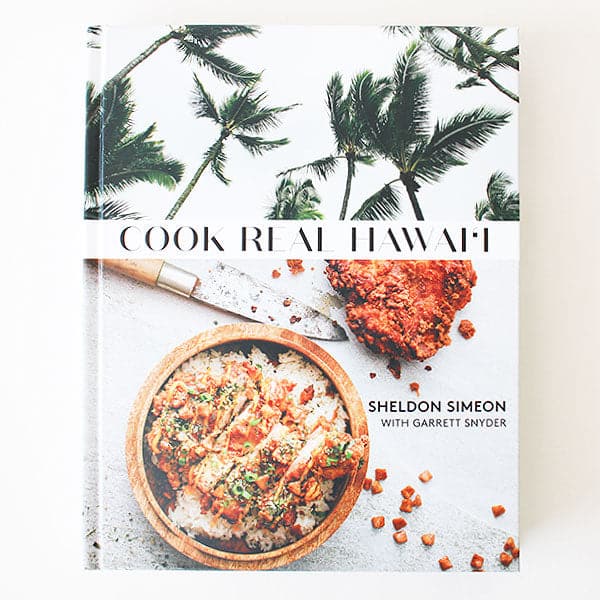 A white book cover with palm trees and a vibrant meal in a bowl along with with text that reads, "Cook Real Hawai'i".