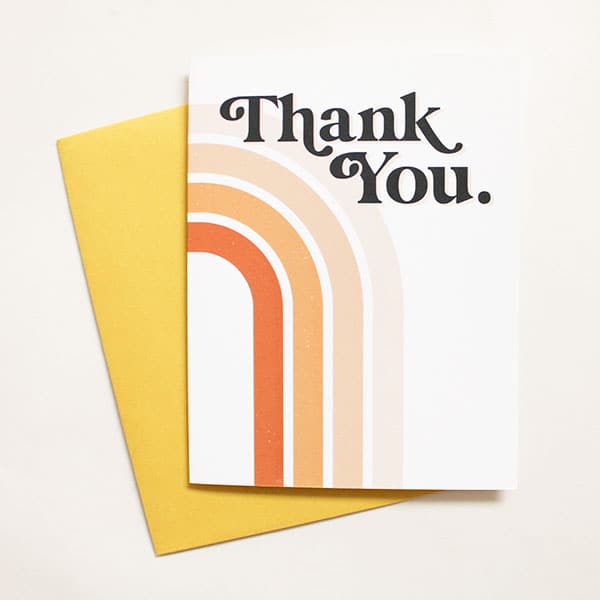 A 70&#39;s style Thank you card. &quot;Thank you&quot; in black retro lettering, and behind the text is a rainbow of orange, peach and tan colors. Comes with a yellow envelope.