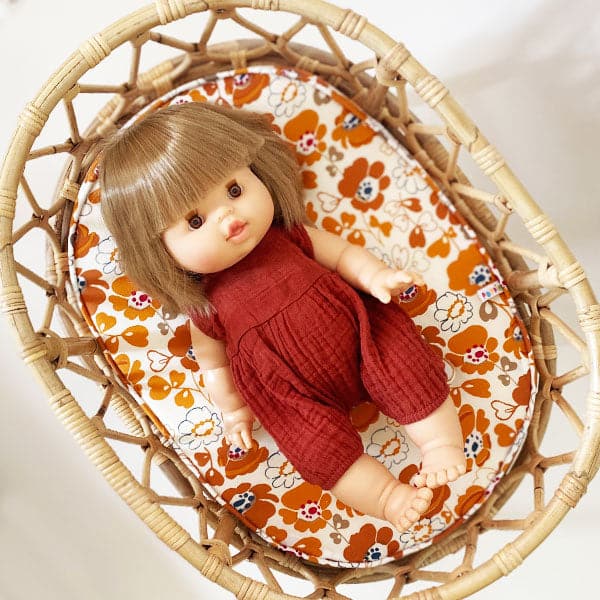 Baby doll toy with a blonde bob haircut sitting inside of bohemian crib in a deep red outfit. Both items sold separately.
