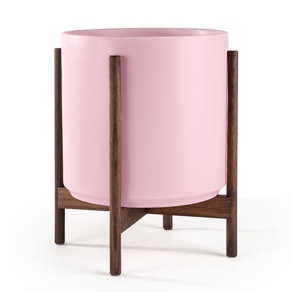 This cylinder pot is pastel pink and sits within four spokes of a dark walnut wood plant stand, standing about 5.5 inches from the ground.