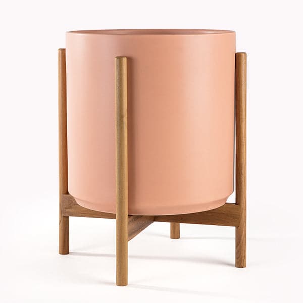 This cylinder pot is a peachy color and sits within four spokes of a neutral wood plant stand, standing about 5.5 inches from the ground.