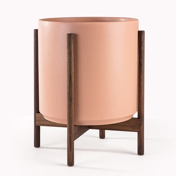 This cylinder pot is a peachy color and sits within four spokes of a dark wood plant stand, standing about 5.5 inches from the ground.