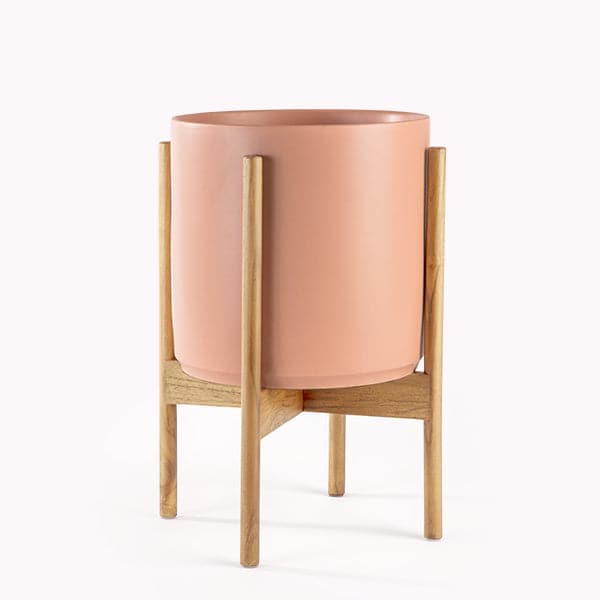 This cylinder pot is a peachy color and sits within four spokes of a light wood plant stand, standing about 7 inches from the ground.