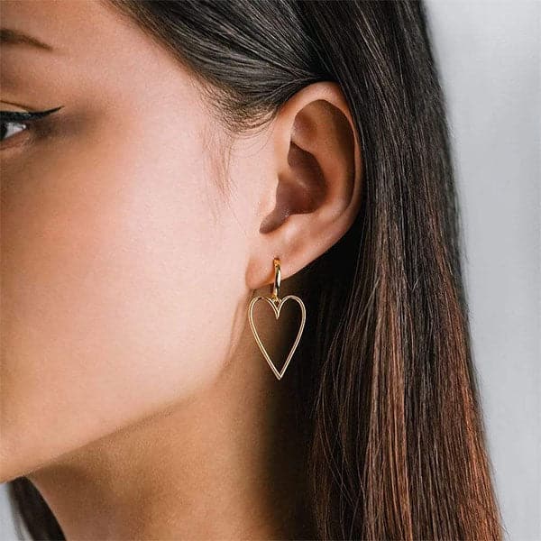 A pair of gold hoop earrings with a larger hold heart shape hoop attached to that worn here on a model's ear.