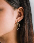A pair of gold hoop earrings with a larger hold heart shape hoop attached to that worn here on a model's ear.