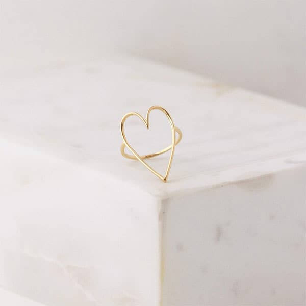 A thin gold ring with a thin gold wired heat shape with the center left open and photographed here on a marble block.