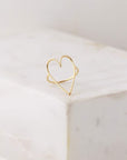 A thin gold ring with a thin gold wired heat shape with the center left open and photographed here on a marble block.