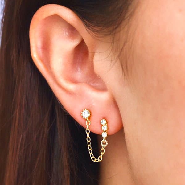 On a model&#39;s ear is a stud earring with a chain connecting to another stud earring. 
