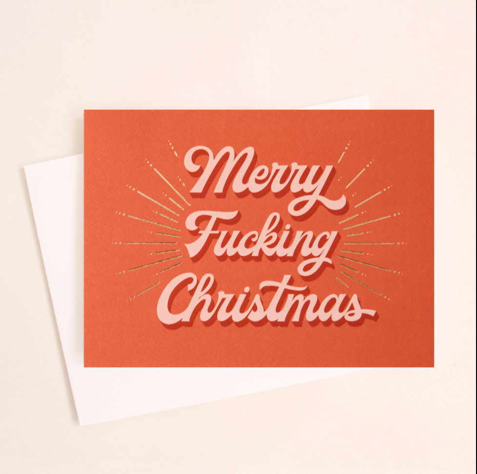 Red card that reads &#39;Merry Fucking Christmas&#39; in soft pink lettering with dark red shadowing. A gold foil burst detailing beams from the text