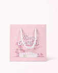 A cool toned pink paper gift bag with a graphic of a midcentury home in front of palm trees along with text that reads, "Warm Holiday Wishes" on the large size and "Merry Christmas" on the smaller one.