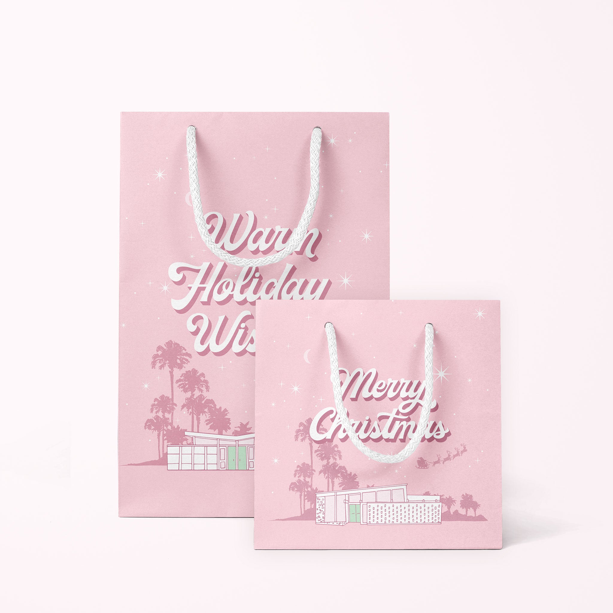 A cool toned pink paper gift bag with a graphic of a midcentury home in front of palm trees along with text that reads, "Warm Holiday Wishes" on the large size and "Merry Christmas" on the smaller one. 