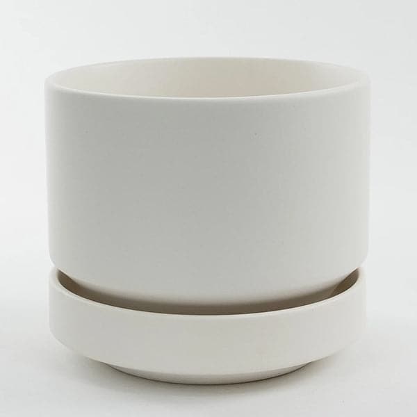 In front of a white background is a round white pot with a matching tray. The tray tapers at the bottom. 