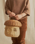 A natural colored rattan mushroom house basket with a handle on the top, a little arched door and square windows.