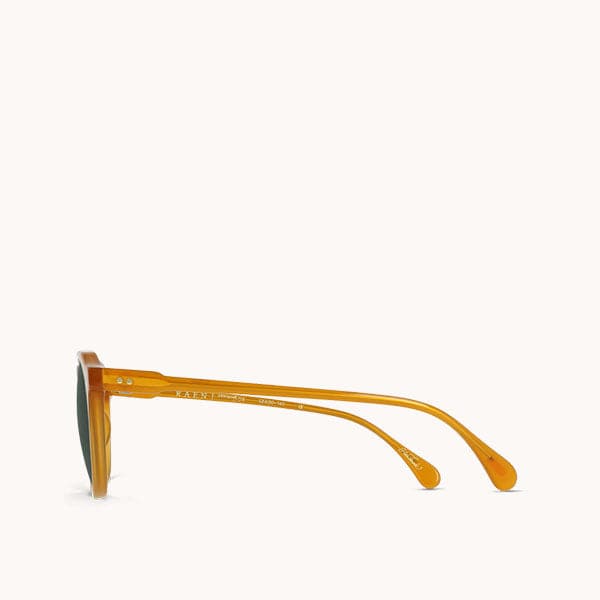 In front of a white background is the side view of a pair of round, orange sunglasses. 