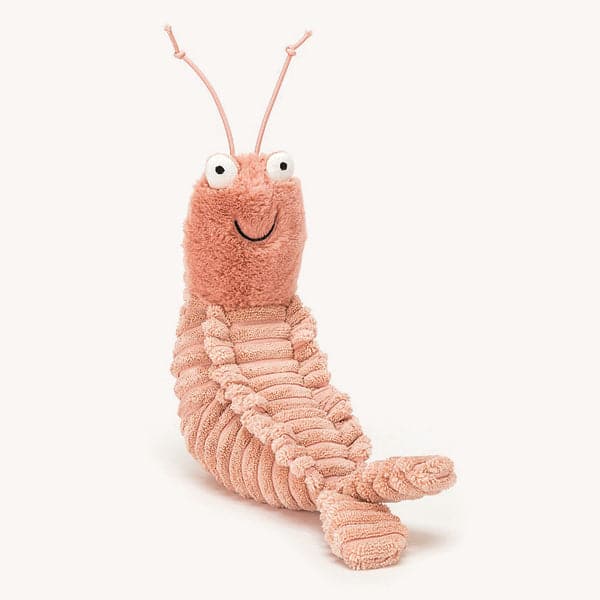 In front of a soft pink background is a stuffed shrimp. The long body of the shrimp is light pink. On the bottom end is two little fins. On top is a pink fuzzy head with two large eyes and a black smile. There are two long pink antennas on top of his head. 