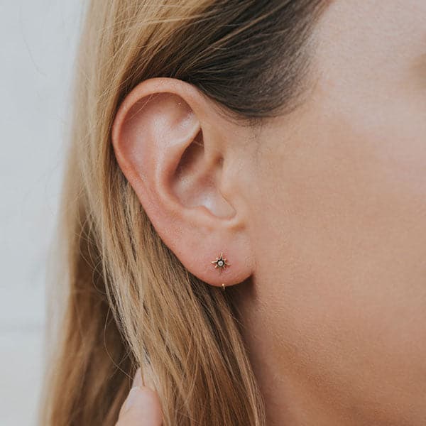 In this picture is a close up of a person’s ear. On the front of her ear is a gold star with a clear, crystal in the middle. There is a gold hoop the starts in the back and loops up from the bottom of her ear. 