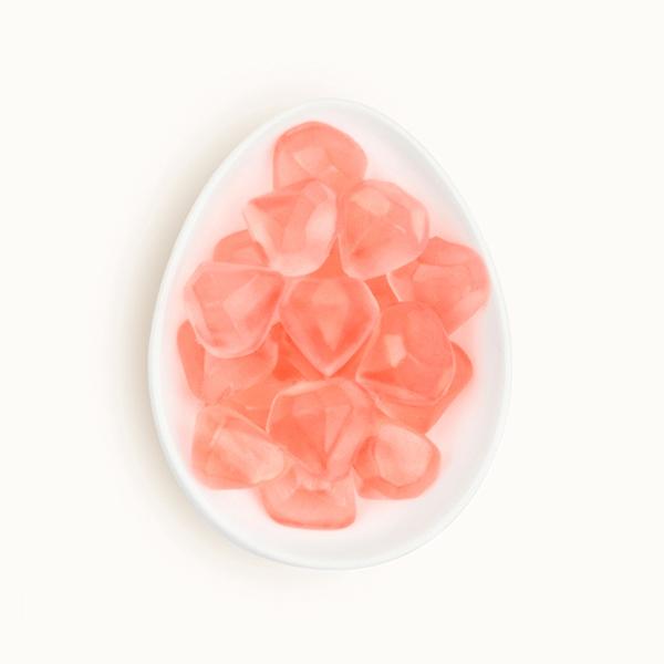 Birds eye view of a white egg shaped dish. The dish is filled with clear pink diamond shaped gummies.