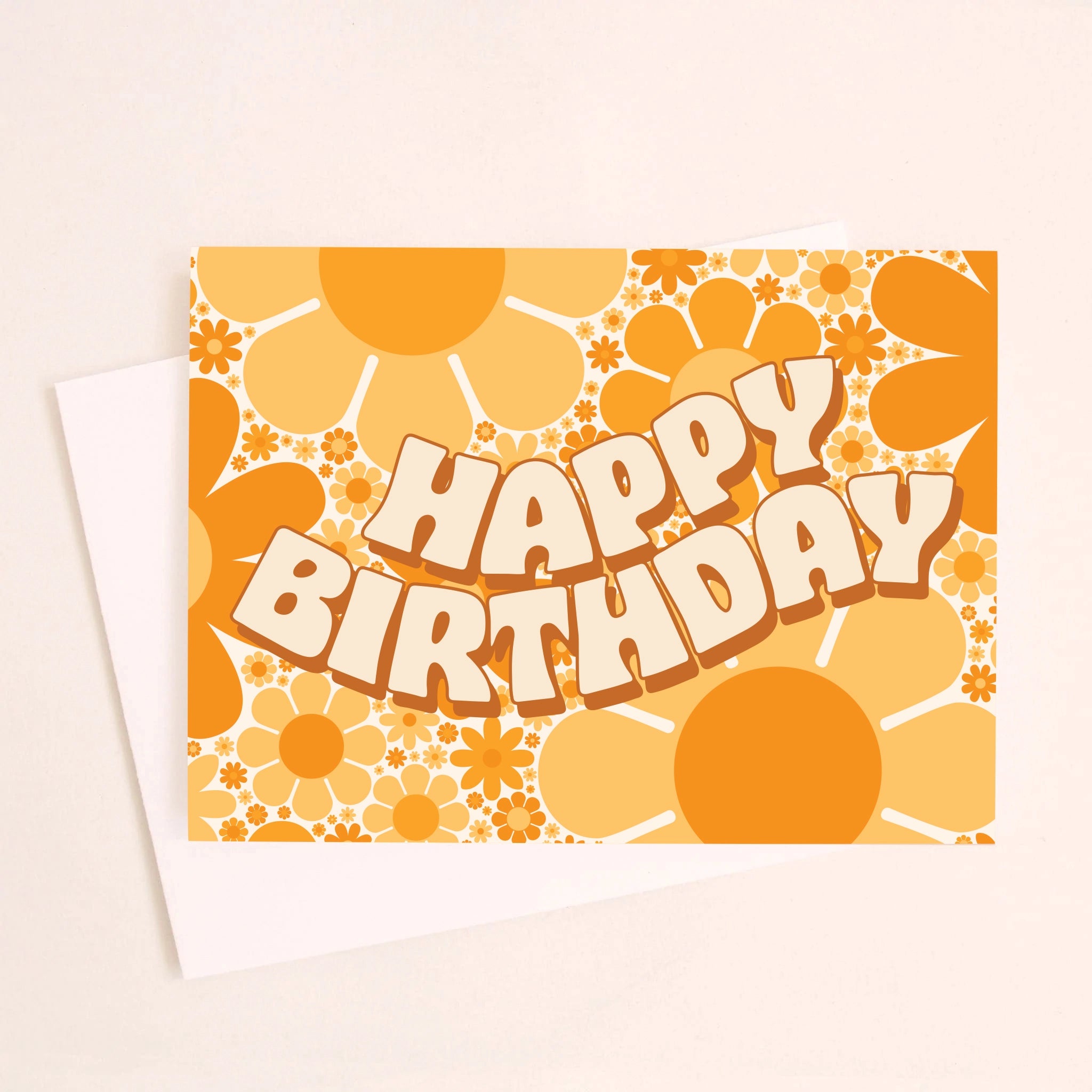 On a cream background is a card with a yellow and orange daisy print and wavy cream text in the center that reads, &quot;Happy Birthday&quot; alongside a white envelope.