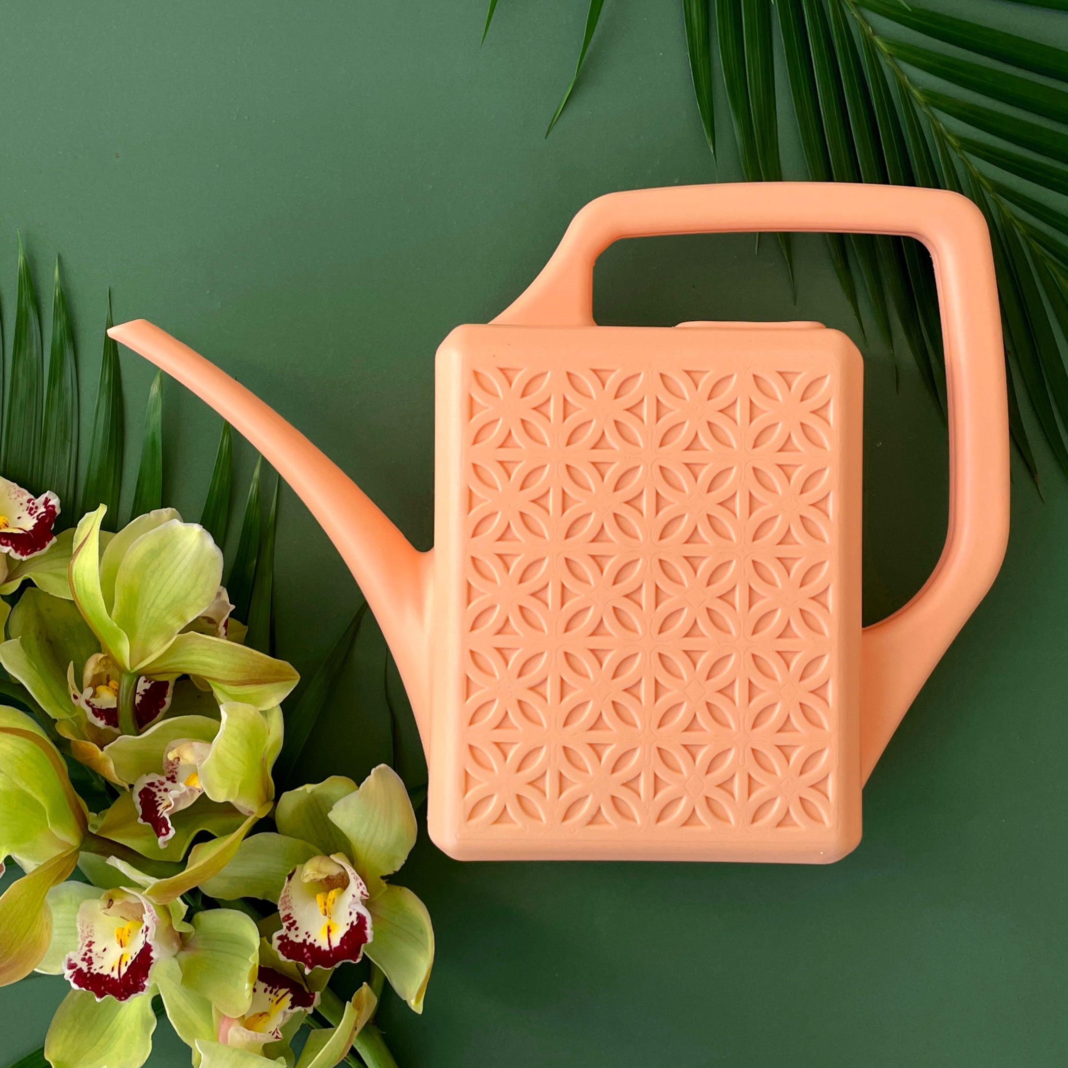 A peach plastic watering can with a narrow spout and square handle and a rectangle breeze block design on the sides. 