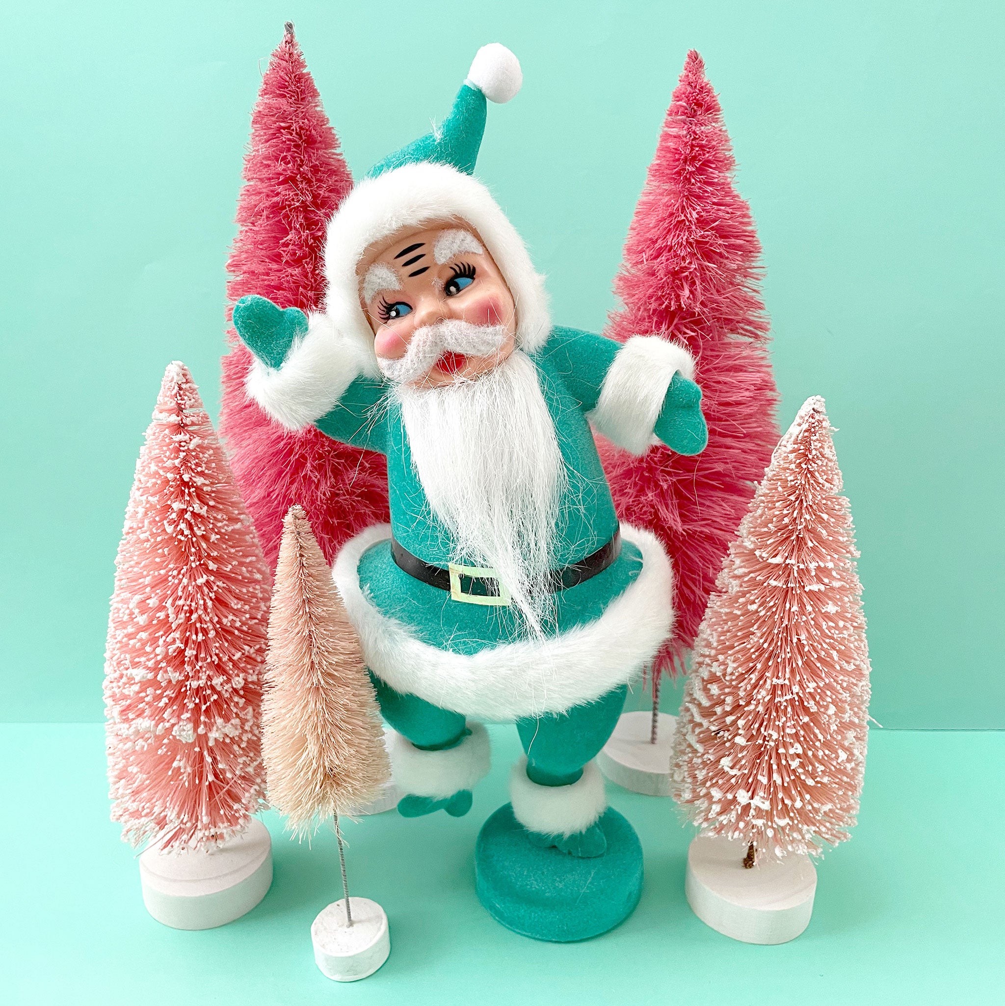 A plastic Santa figurine with a teal suit on with fuzzy cuffs and hat.