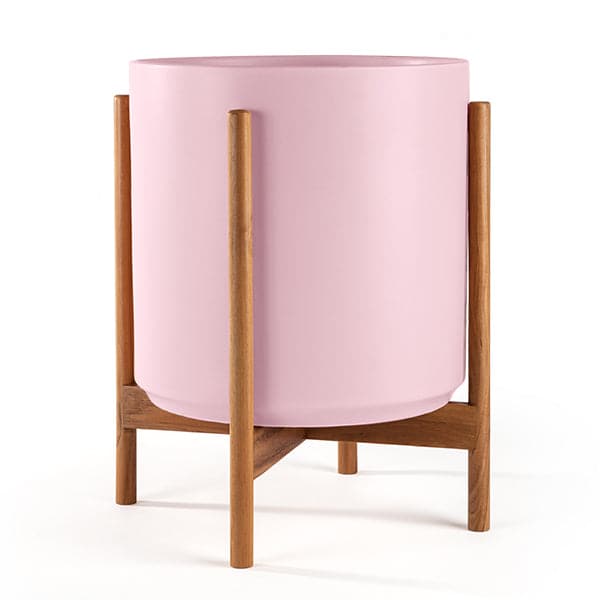 This cylinder pot is pastel pink and sits within four spokes of a neutral wood plant stand, standing about 5.5 inches from the ground.