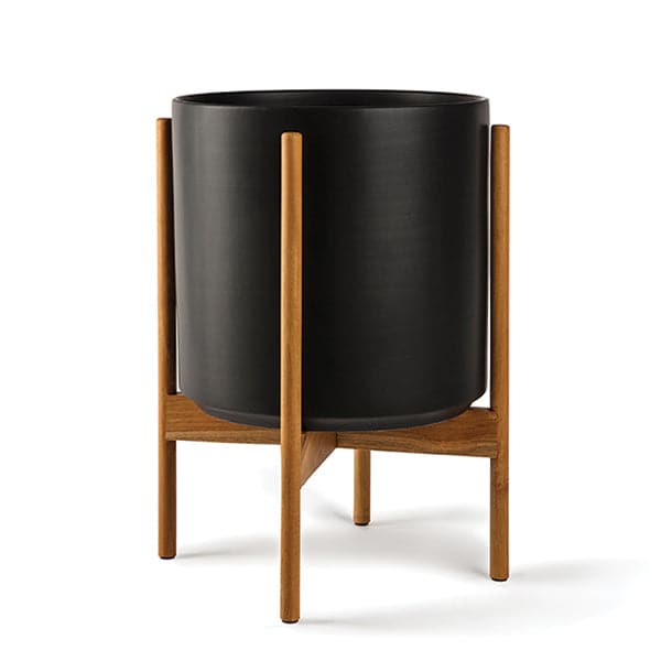 This 5 gallon, cylinder pot is solid black and sits within four spokes of a pecan wood plant stand, standing about 7 inches from the ground. 