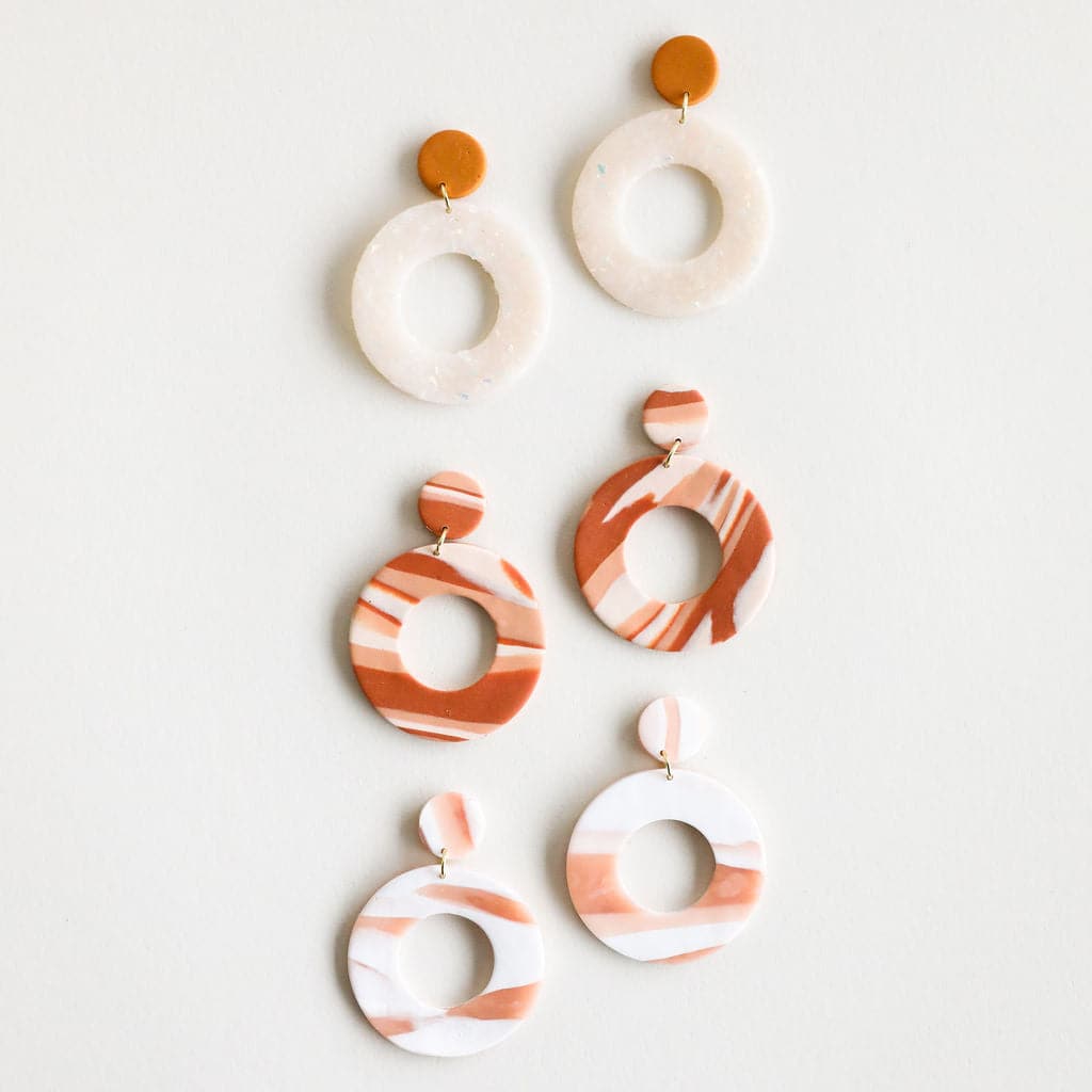 Three sets of clay earrings with a duel circle design, one open and the other larger and open in the center along with a straight post backing. Each pair of earrings sold separately. The colors ways range from mustard yellow and cream, to rust red and cream to salmon pink and white. 