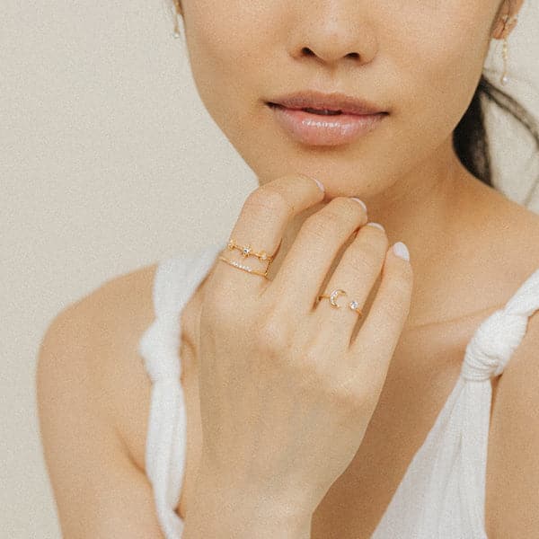 A gold ring with an open front that features a cubic zirconia on one end and a crescent moon on the other, photographed worn on a models hand.