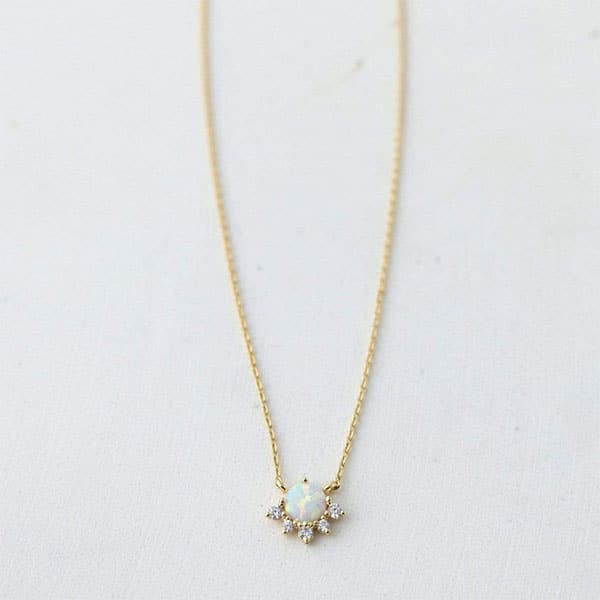 A dainty gold necklace with a round opal pendant in the center that is lined with cz stones around the bottom edge.