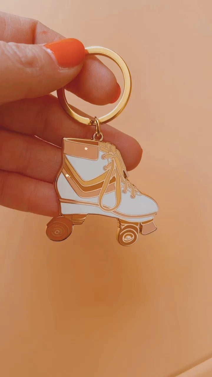 A metal roller skate keychain with orange wheels, and a white boot with pink, orange and yellow stripes in the center along with yellow shoelaces and a gold keychain hoop.