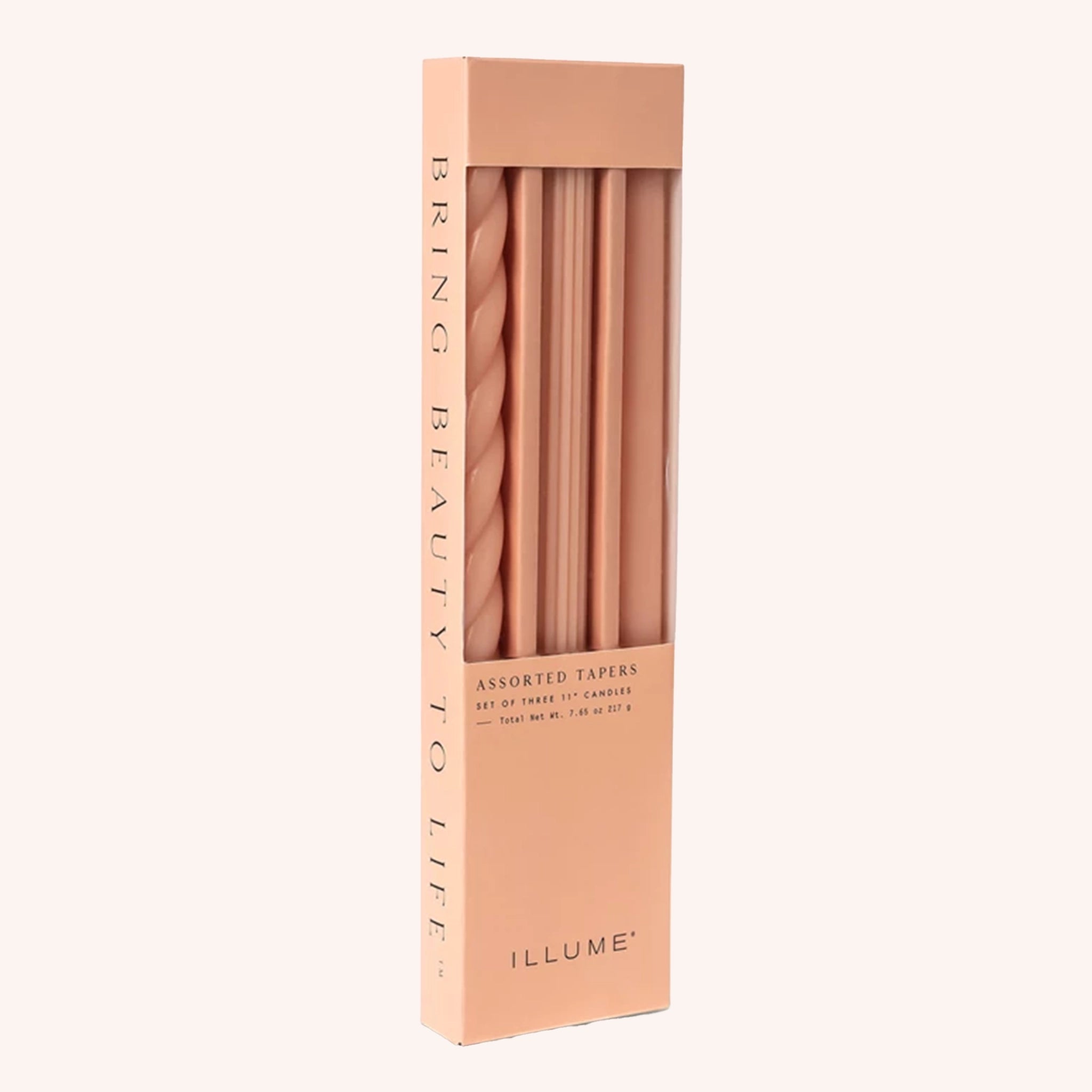 A box of three peach colored tapered candles, one has a twisted design, another has a vertically ribbed detail and the last candle is smooth. The box reads, "Illume Bring Beauty To Life Assorted Tapers".