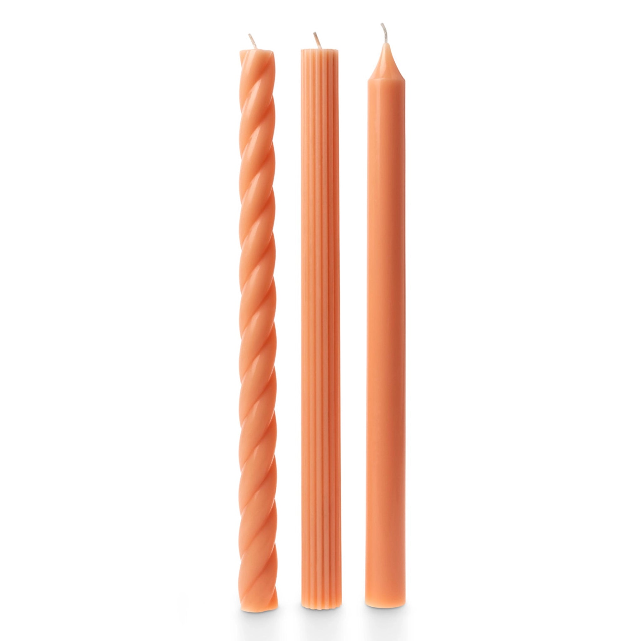 Three peach colored tapered candles, one has a twisted design, another has a vertically ribbed detail and the last candle is smooth.