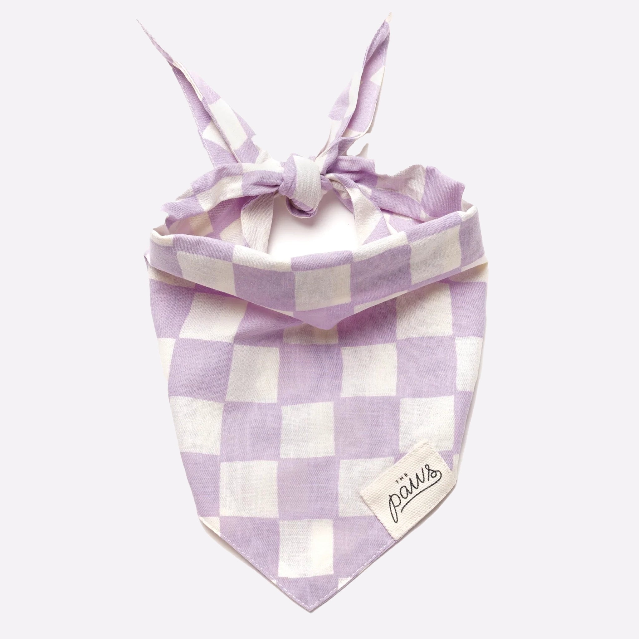 A lavender and white checkered pet bandana with a tie back and a small label on the front that reads the brand&#39;s name, &quot;The Paws&quot;.