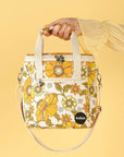 Photographed in front of a yellow background is a mini cooler with cream straps and 70's style yellow and orange floral print.