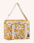 Photographed in front of a yellow background is a picnic bag with cream straps and 70's style yellow and orange floral print.