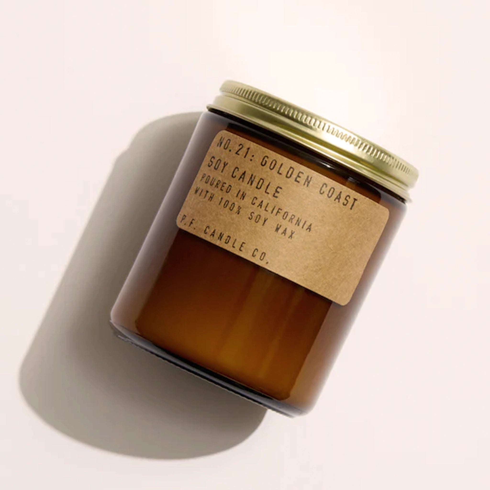 Candle features amber glass with a gold lid. The label is kraft paper with typewriter font that reads "No.21: Golden Coast Soy Candle Handmade in California with 100% Soy Wax. P.F. Candle Co."