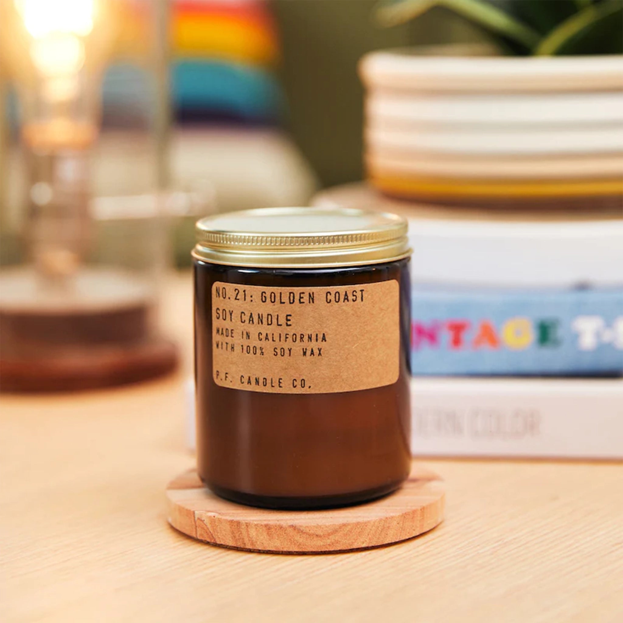 Candle features amber glass with a gold lid. The label is kraft paper with typewriter font that reads &quot;No.21: Golden Coast Soy Candle Handmade in California with 100% Soy Wax. P.F. Candle Co.&quot;
