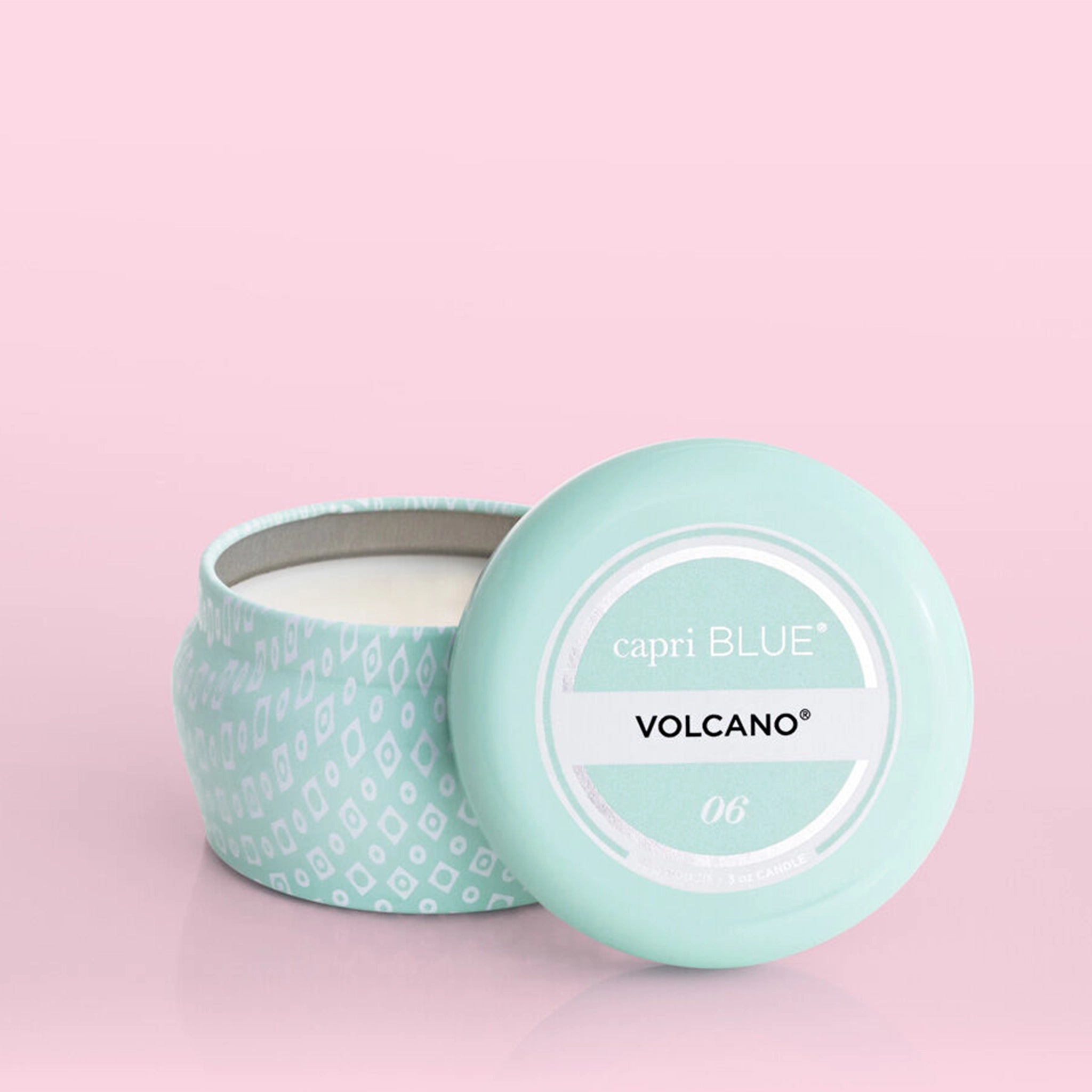 A small blue tin candle with white wax and a white diamond repeating pattern on the outside of the tin. Comes with a matching blue lid that reads, "Capri Blue Volcano".