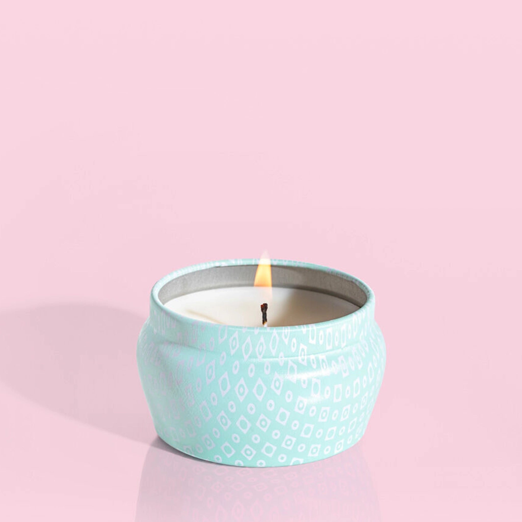 A small blue tin candle with white wax and a white diamond repeating pattern on the outside of the tin. Comes with a matching blue lid that reads, &quot;Capri Blue Volcano&quot;.