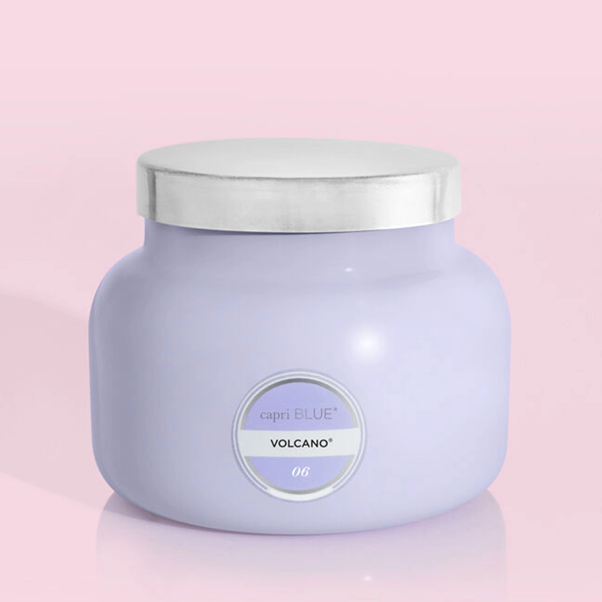 The larger of the two glass candle jars in a lavender purple shade along with a silver lid and a circle label in the center that reads, "Capri Blue, Volcano 06".