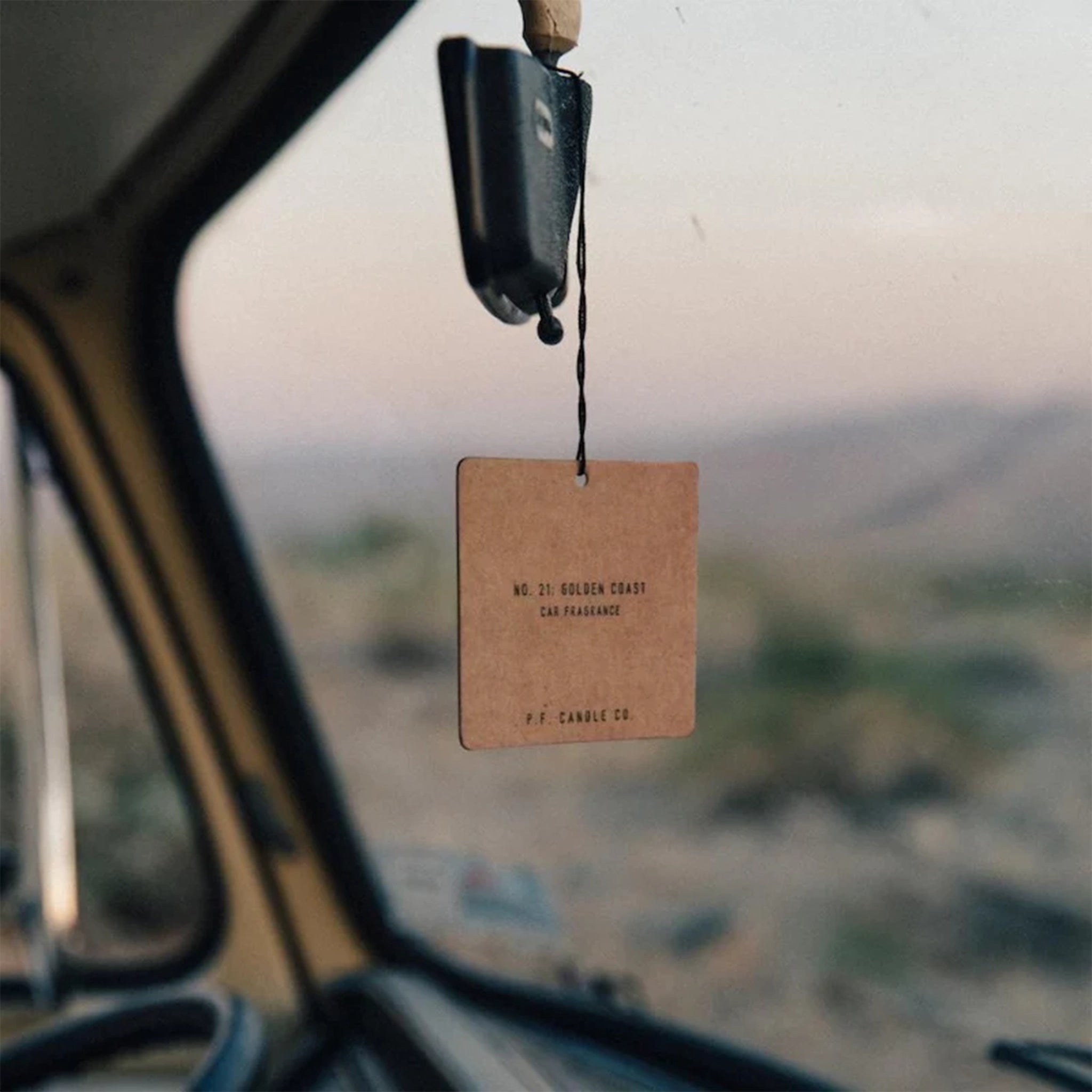 The square cardboard car fragrance hanging on the rear view mirror of a car. 
