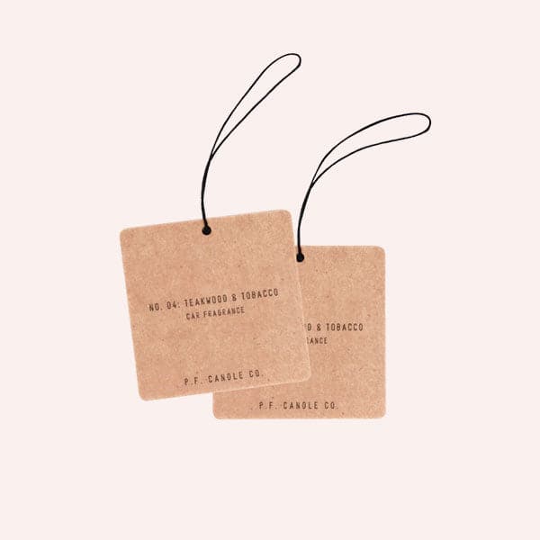 Two cardboard square air fresheners with a black elastic loop for hanging and small black text that reads, "No. 40: Teakwood & Tobacco Car Freshener, P.F. Candle Co".