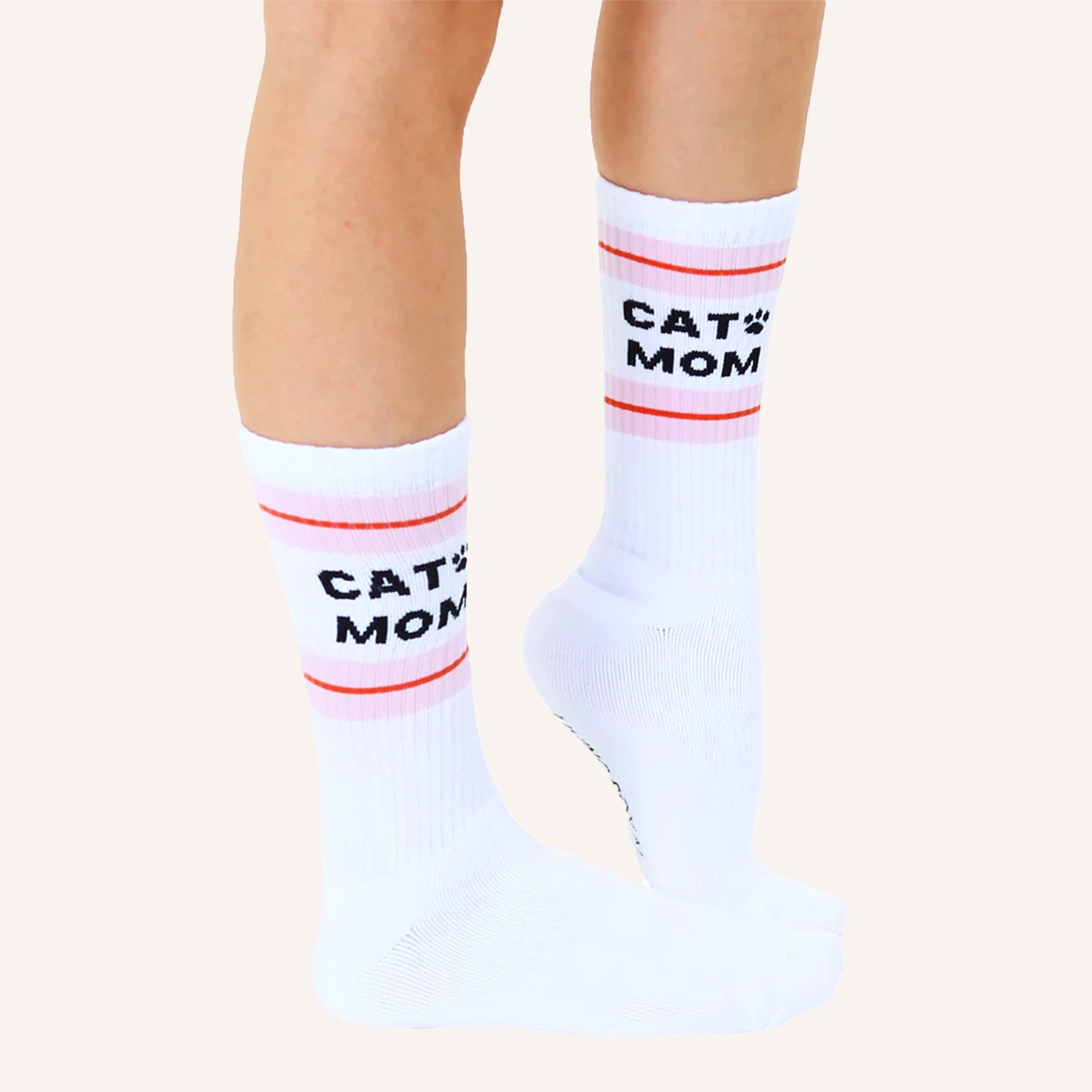 White crew socks with a pink and red striped design at the top along with black text that reads, "Cat Mom" as well as a small black paw print next to the word "cat".
