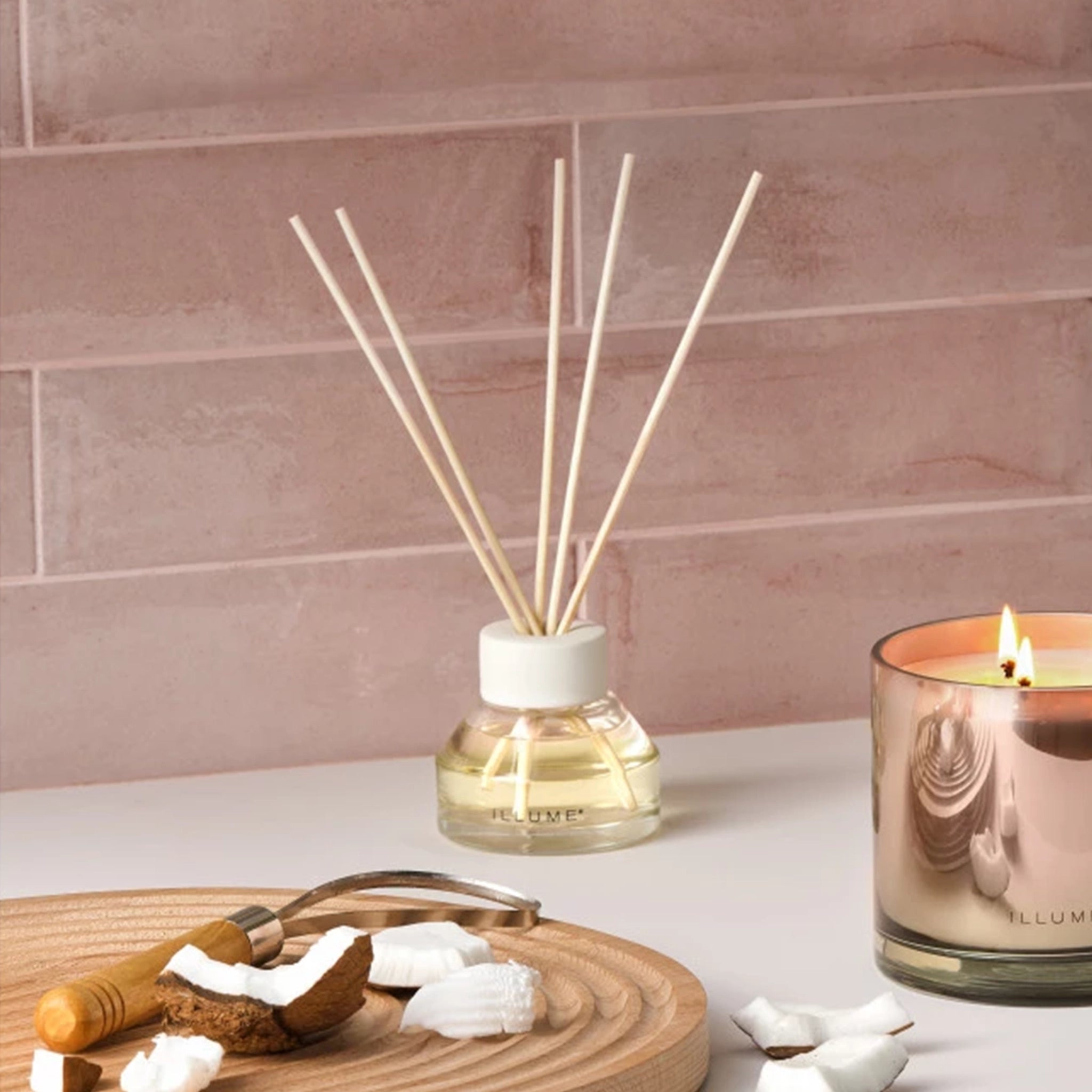 A oil diffuser with a clear glass filled with scented oil a clean cream colored lid and five neutral wood reeds stemming out from the top.