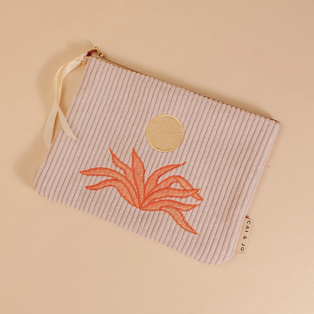 A light pink corduroy pouch with a sun and an orange aloe plant graphic in the center. The pouch has a single zipper going across the top.