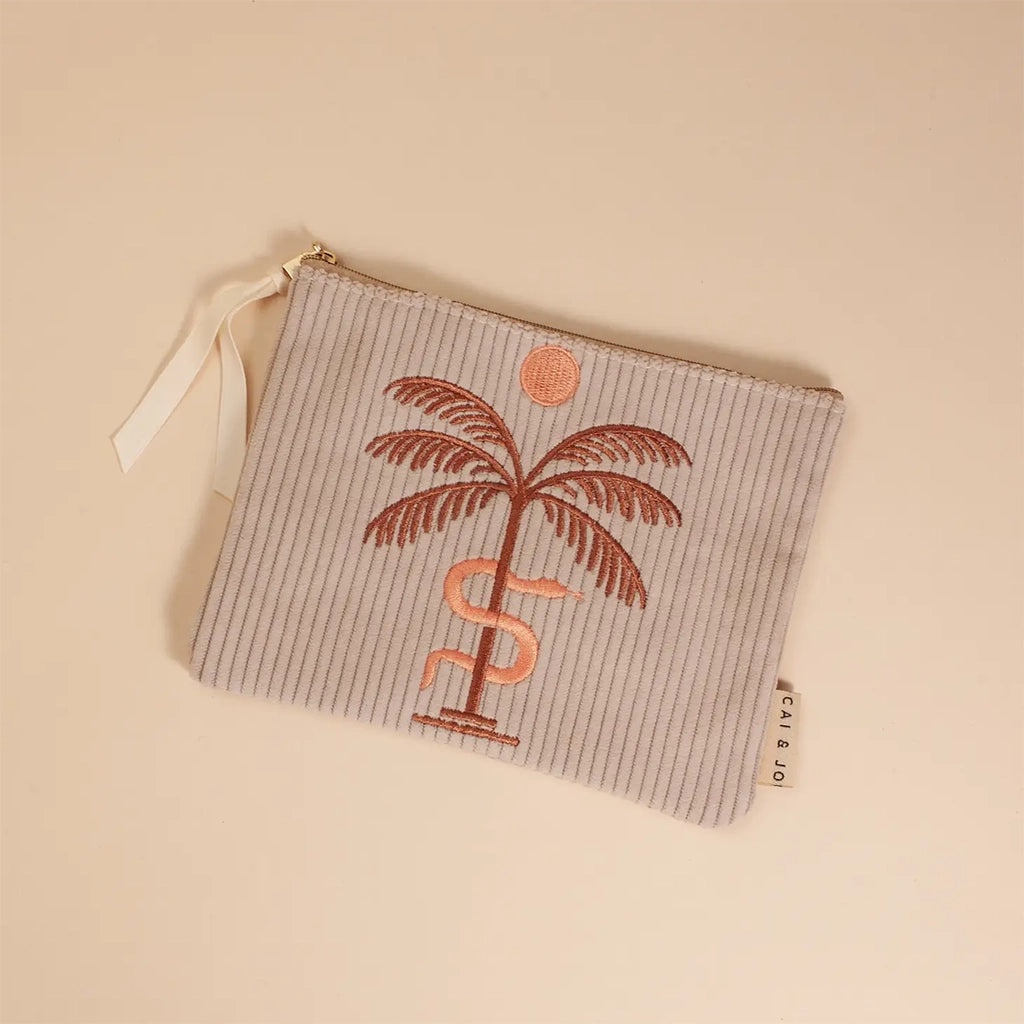A greyish tan corduroy pouch with a single zipper going across the top and a palm tree, snake and sun graphic in the center.