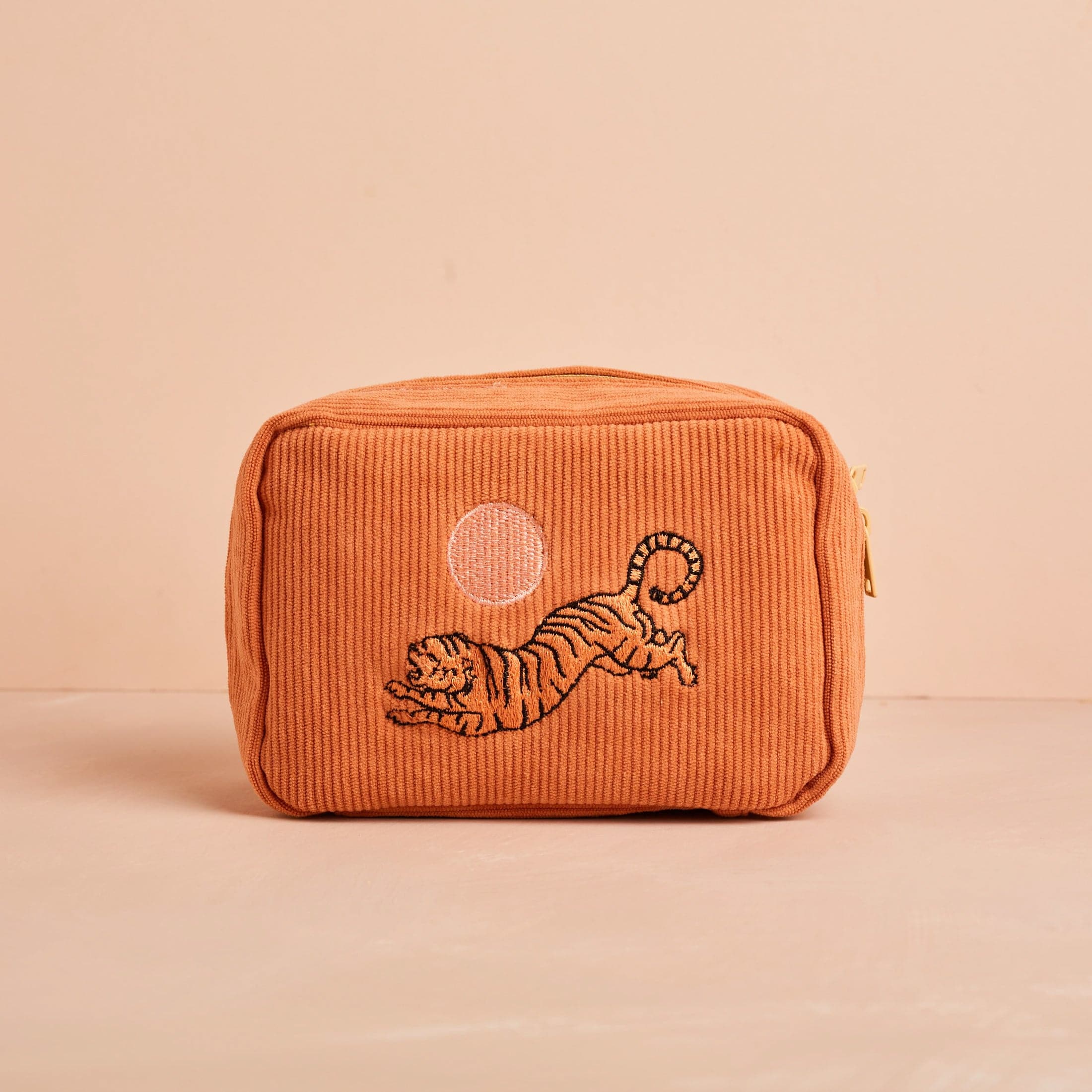 A salmon colored corduroy makeup bag with a tiger design and a pink sun.